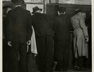 People at counters with registration numbers for transports (source: http://collections.jewishmuseum.cz)